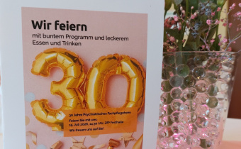 Programm der Jubiläumsveranstaltung mit Blumenschmuck im Hintergrund 