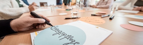 Meetingrunde am Tisch mit Zettel und Beschriftung "Bezugspflege"