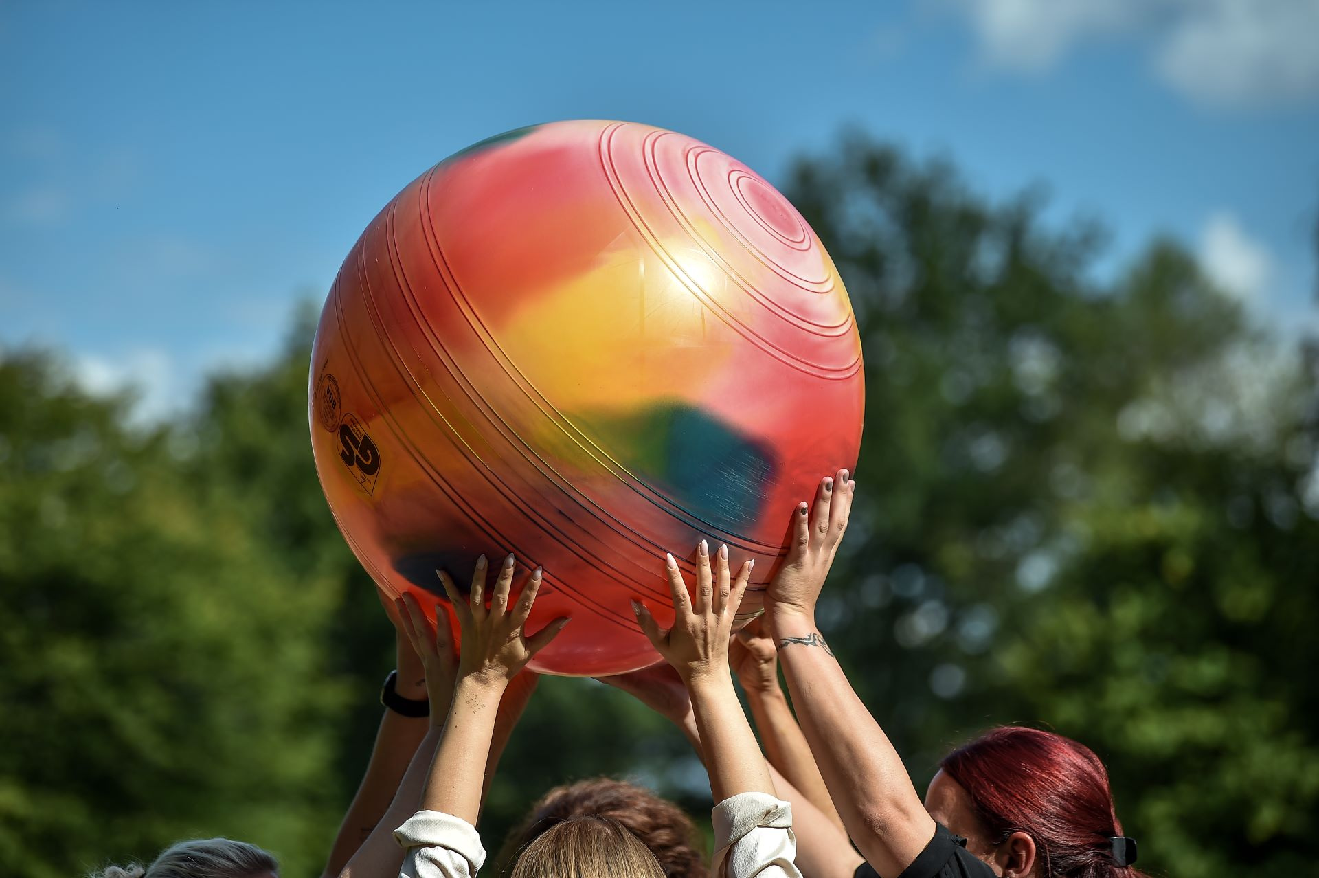 Mehrere Personen strecken gemeinsam einen bunten Gymnastikball in die Höhe